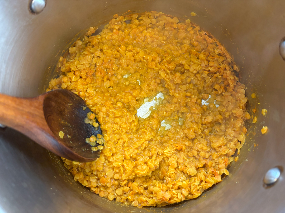 Mashing the dal with a wooden spoon against the pot