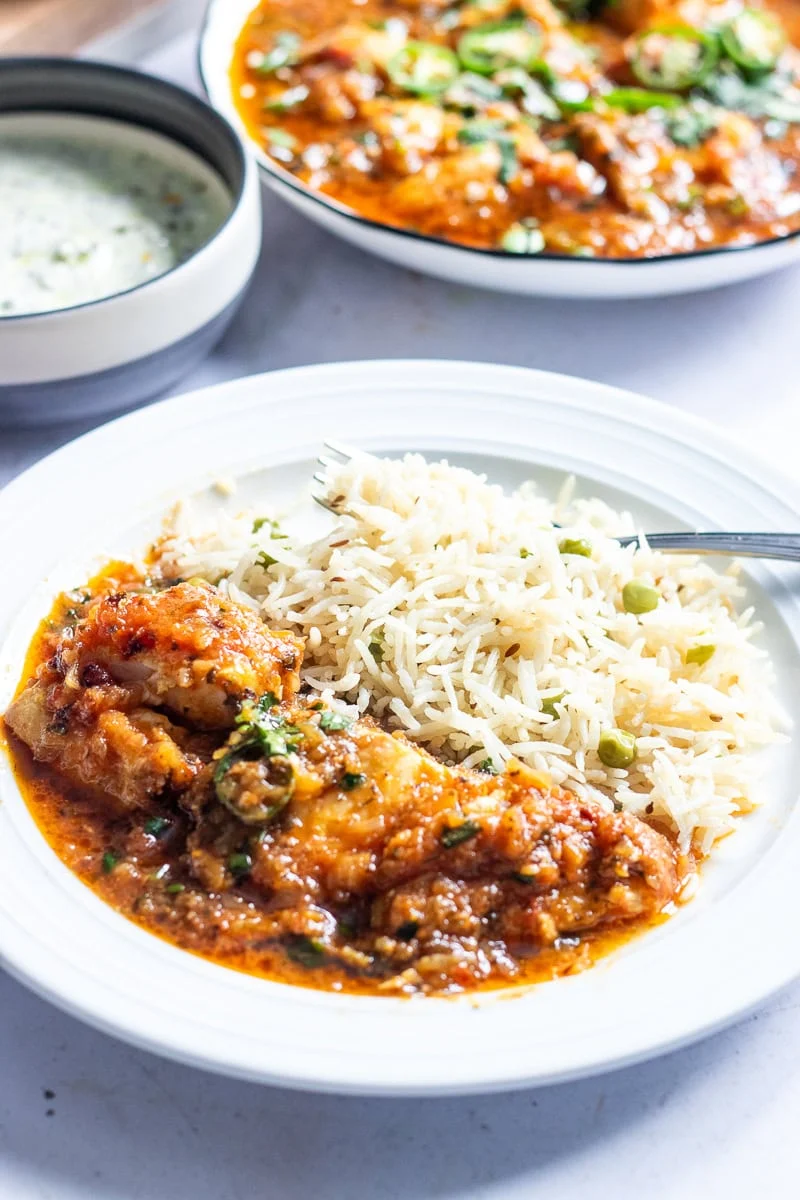 fish ka salan with a pea pilaf in the foreground, a bowl of raita and the dish for  the fish curry in the background