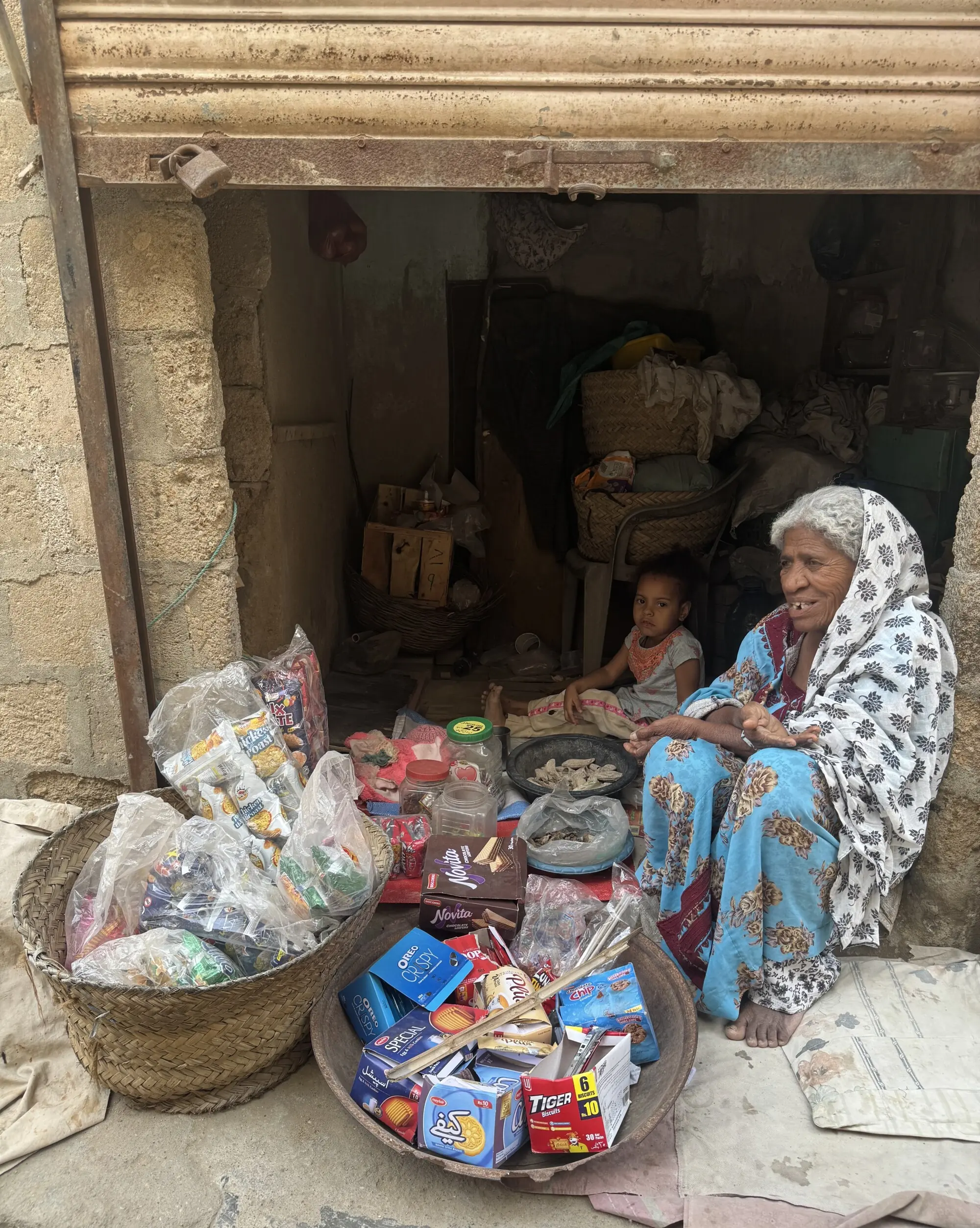 A woman sits with a host of snacks before her, hoping to sell some.