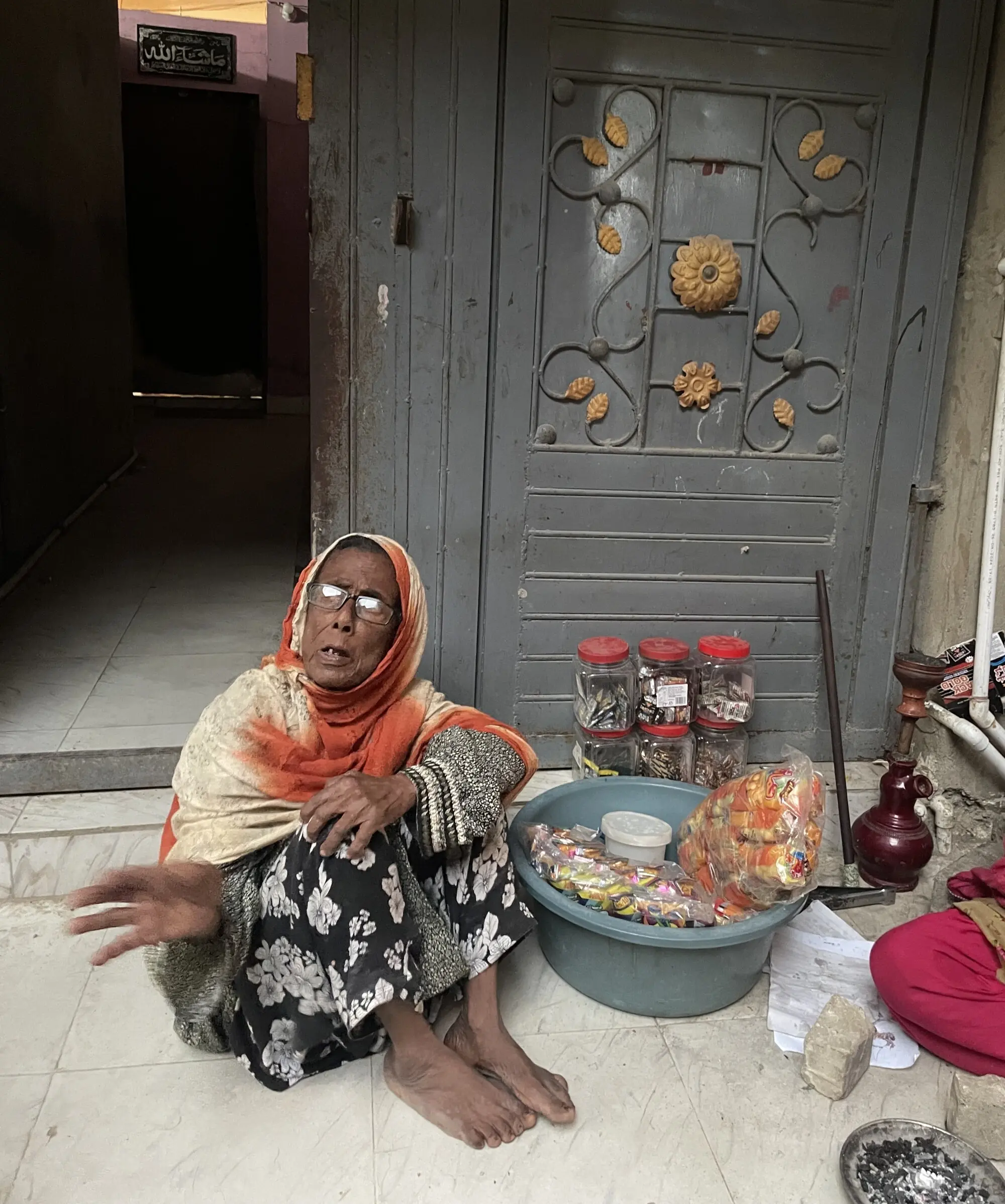 A woman sits outside her home, ready to sell snacks.