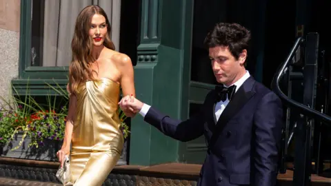 Getty Images Karlie Kloss in a strapless gold dress holding hands with Joshua Kushner emerging from a doorway